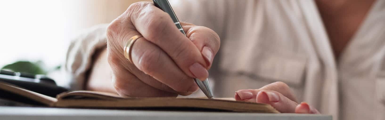 Close-up of a person writing in a notebook with a pen.