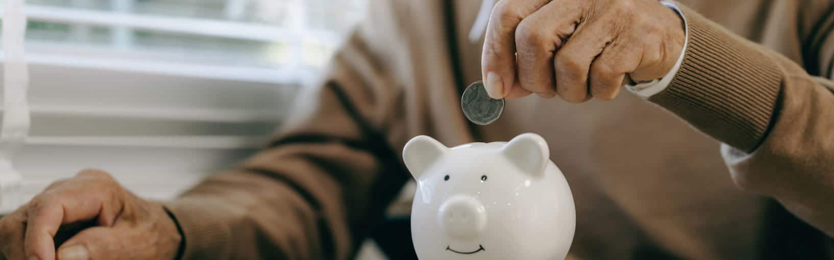 Close-up of a person dropping a coin into a white piggy bank.
