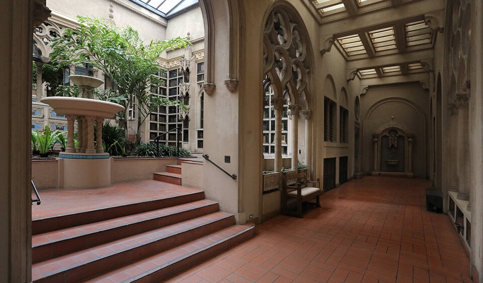Indoor courtyard with plants, fountain, and arched windows in a memorial space.