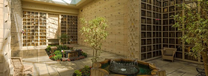Indoor garden with trees, plants, and a fountain inside a memorial space.