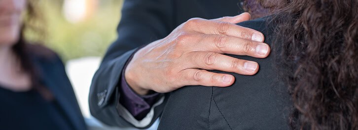 Person placing hand on another person's shoulder during a memorial gathering.