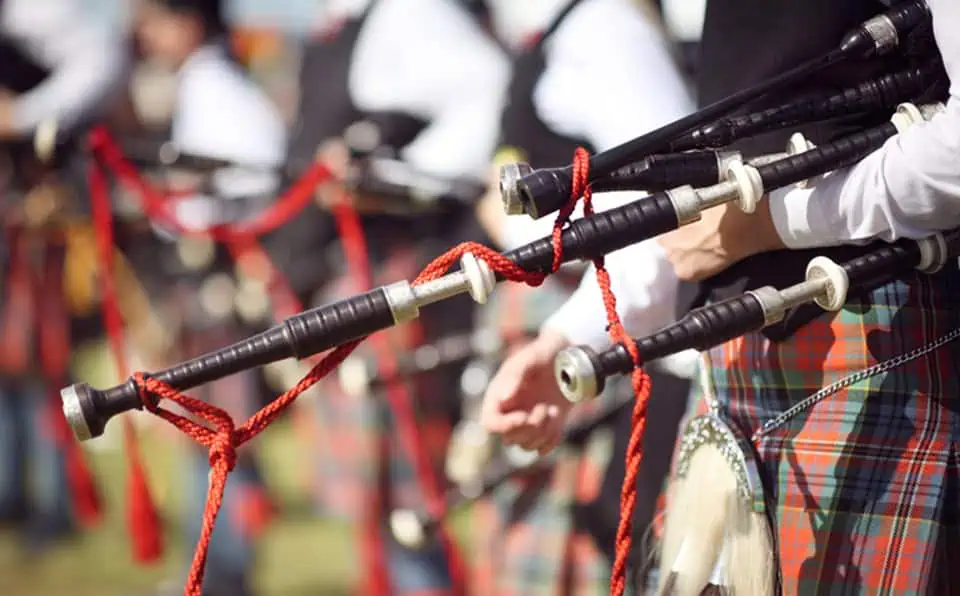 Group of bagpipers in traditional attire playing outdoors.