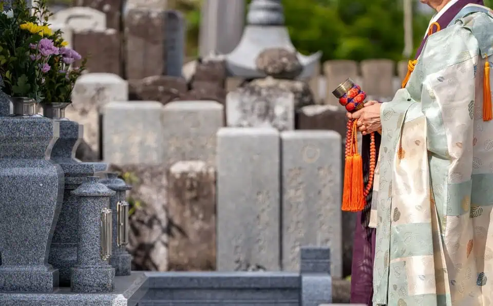 Person in traditional kimono holding prayer beads at cemetery.