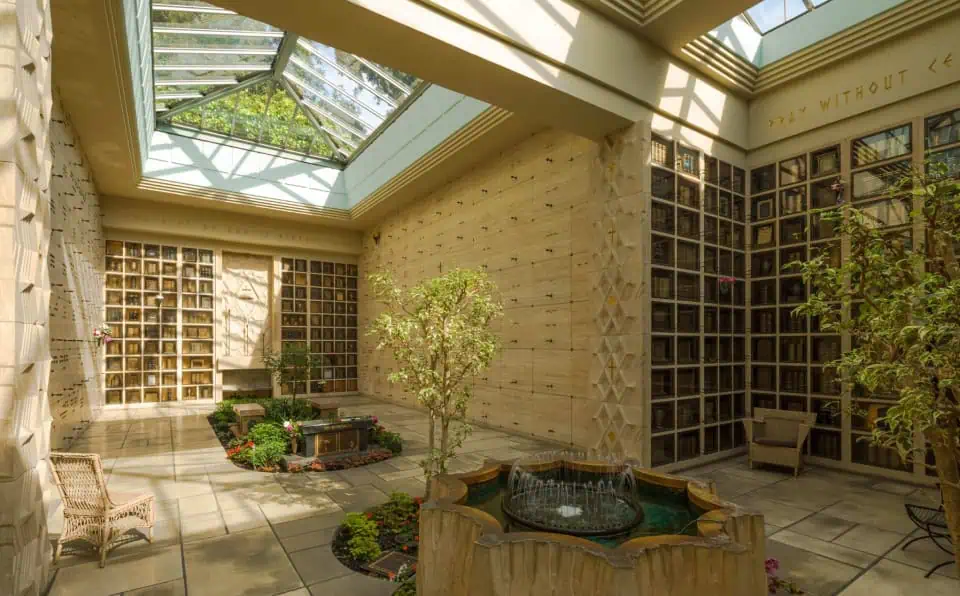 Indoor garden with trees, water feature, and seating inside a memorial building.