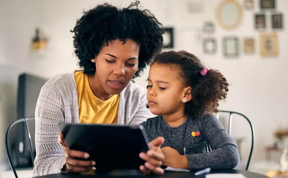 African American woman and young girl looking at a tablet together in a home setting.