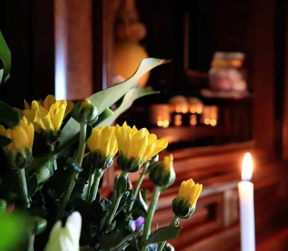 Close-up of yellow flowers and a lit memorial candle in a chapel setting.