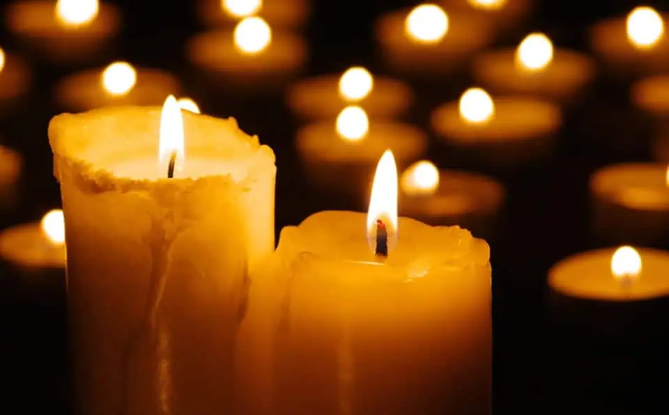 Multiple lit candles with flickering flames in a memorial setting.