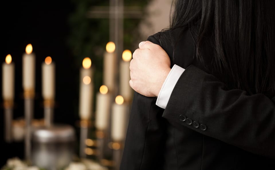 Person embracing another during a memorial service with lit candles in the background.