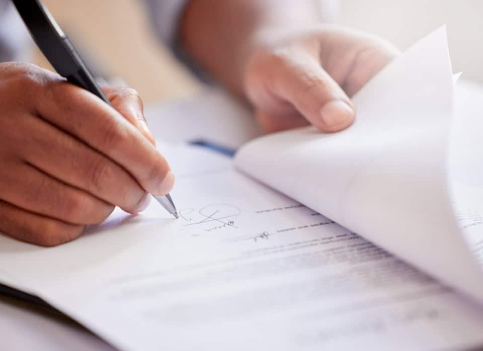 Close-up of hands signing papers for a funeral arrangement.