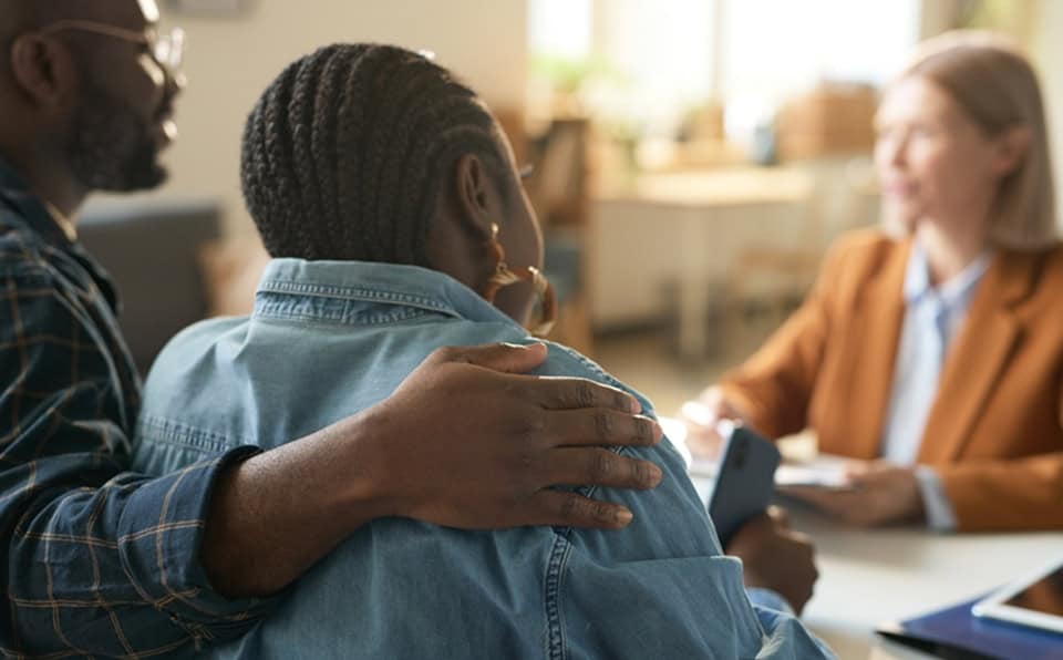 Two people comforting a woman during a counseling session in a bright room.