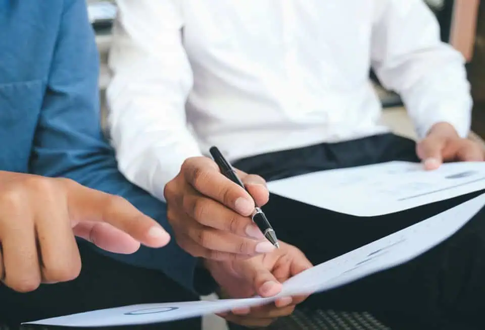 Two people signing legal documents at a table, one holding a pen.