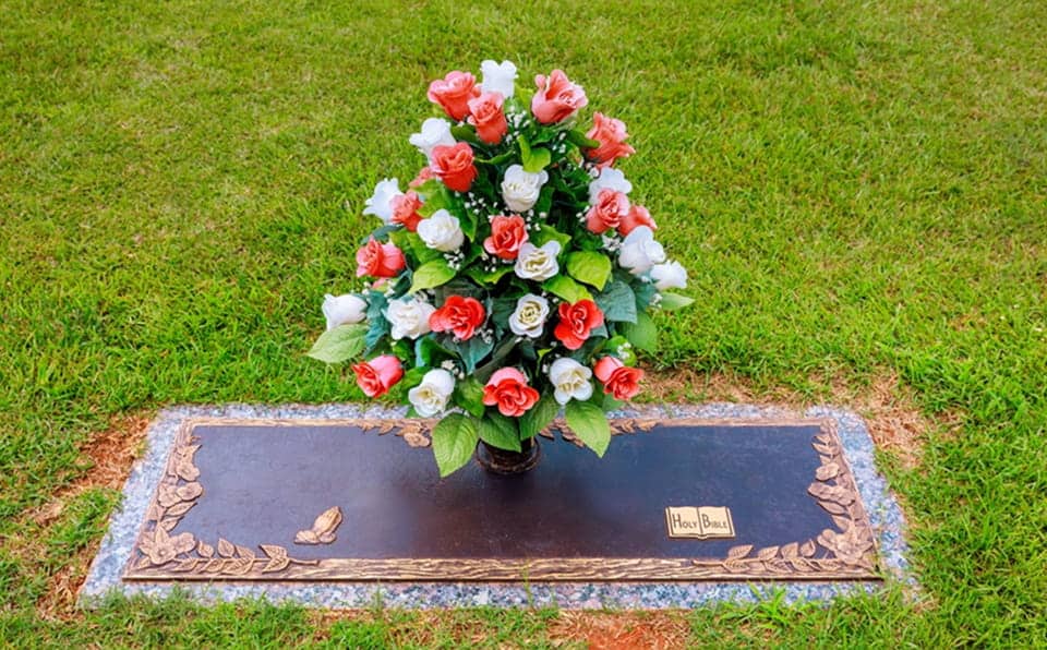 Colorful flower arrangement on a bronze and granite memorial marker in a cemetery.