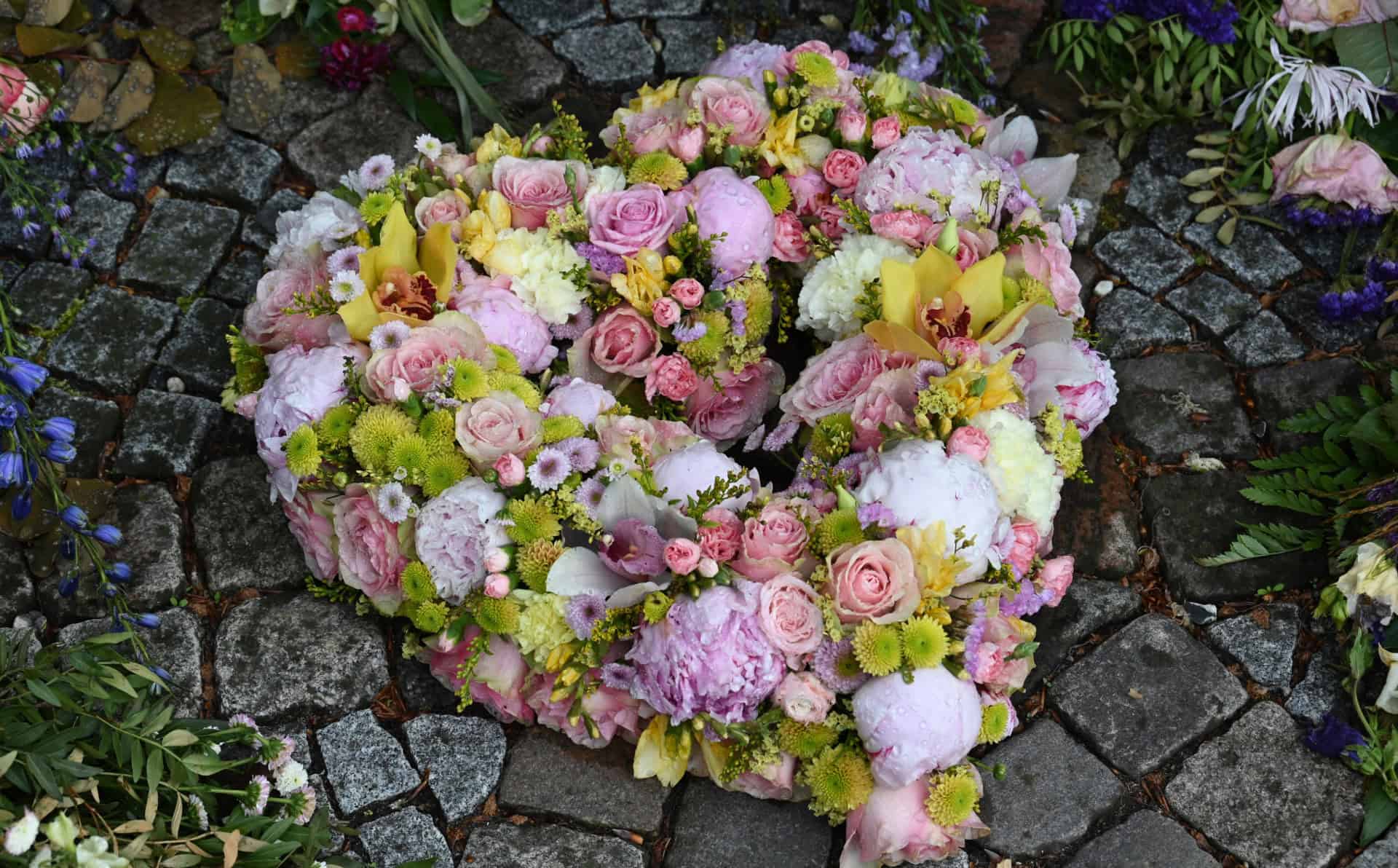 Heart-shaped floral arrangement with pink, yellow, and white flowers on cobblestone ground.