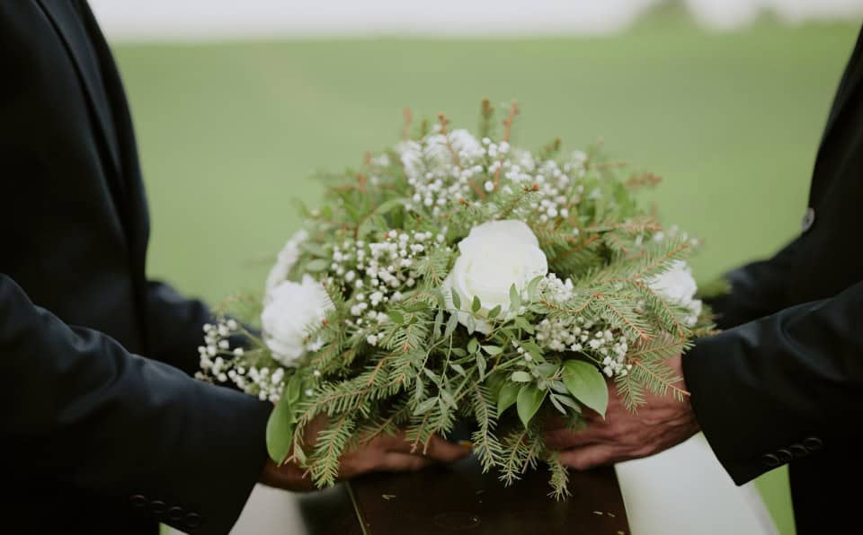 Two people holding a floral arrangement with white roses and greenery.