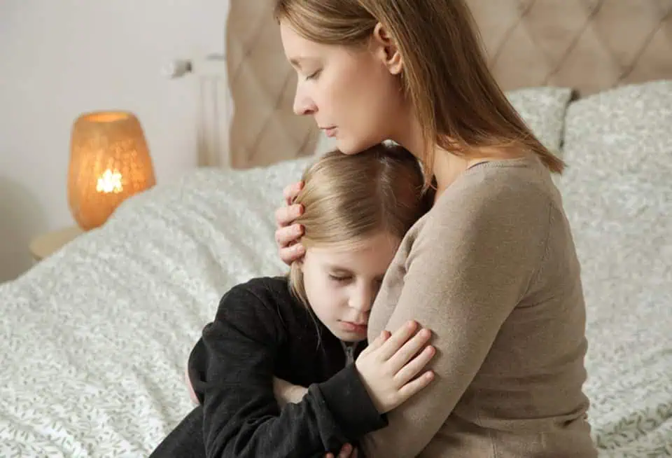 Woman comforting a young girl with a hug in a cozy bedroom.
