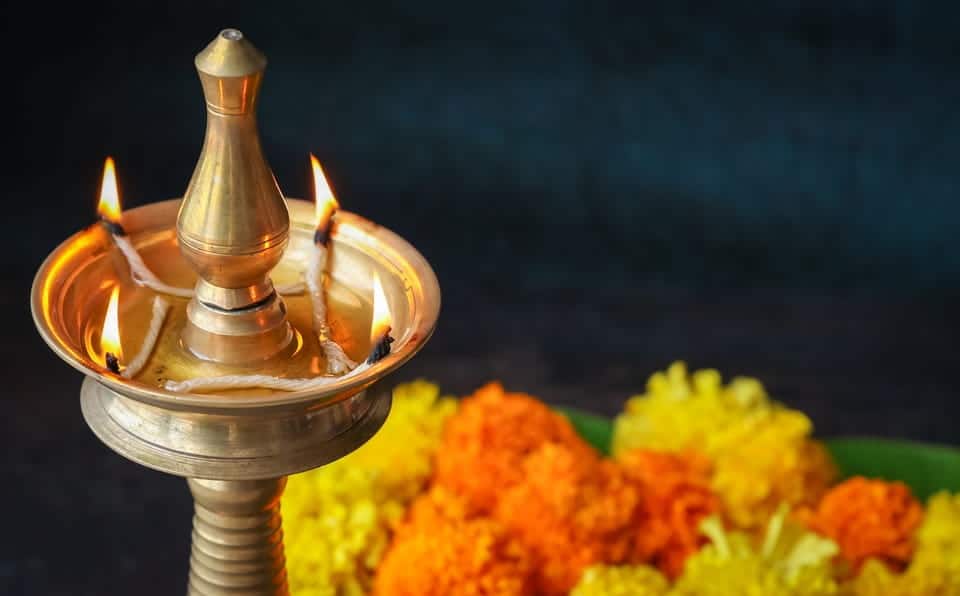 Traditional oil lamp with lit flames, surrounded by marigold flowers.