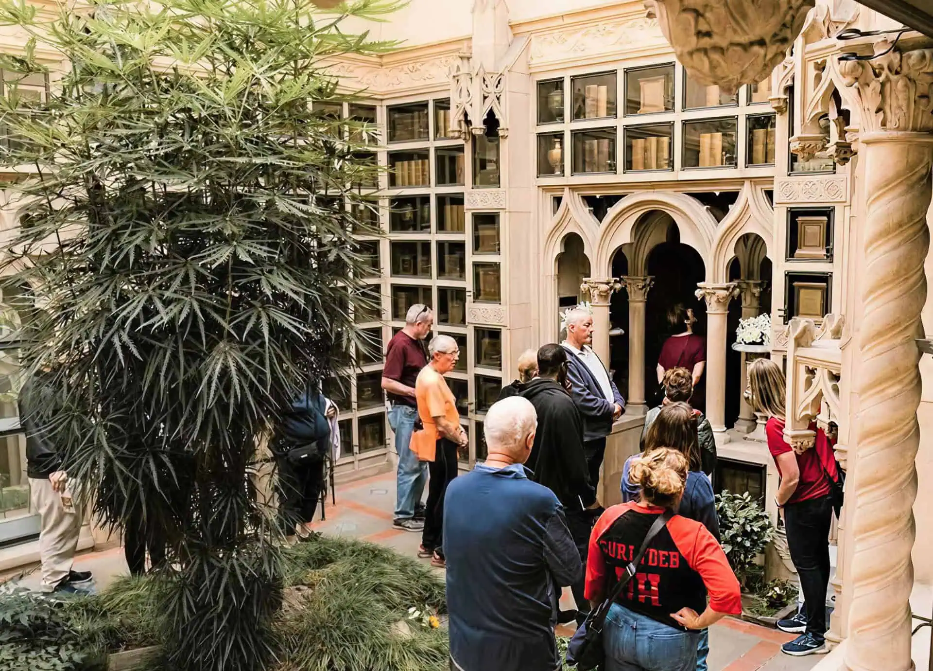 Visitors inside the ornate chapel with detailed architecture and a large plant.