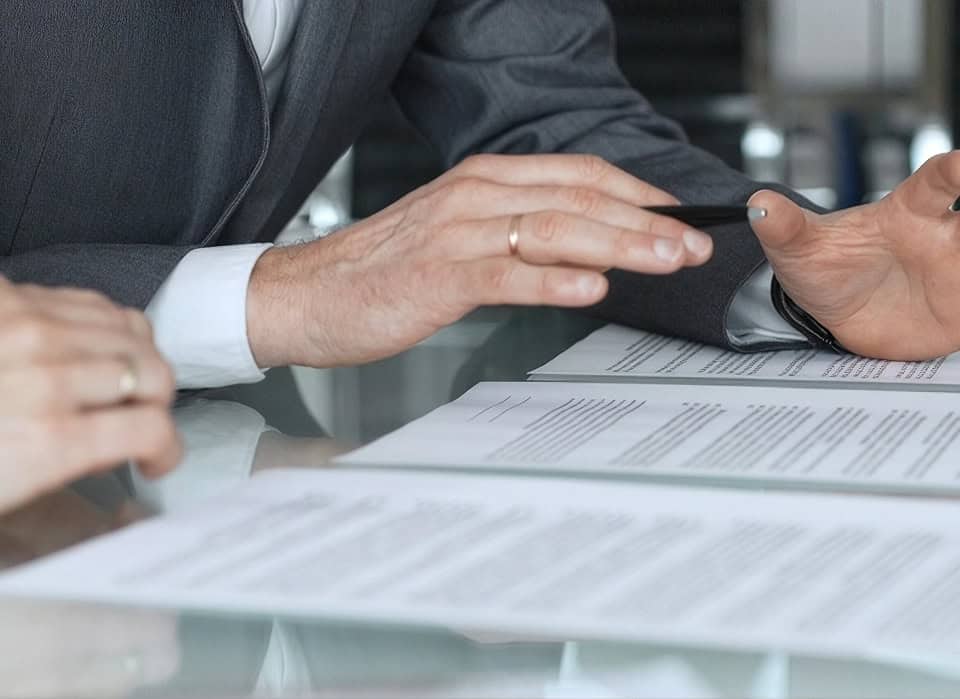 Person signing a death certificate at a desk with documents.