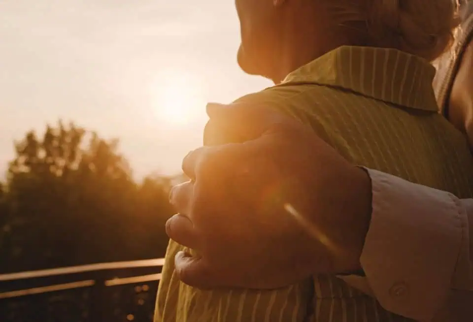 Person being comforted by another during sunset outdoors.