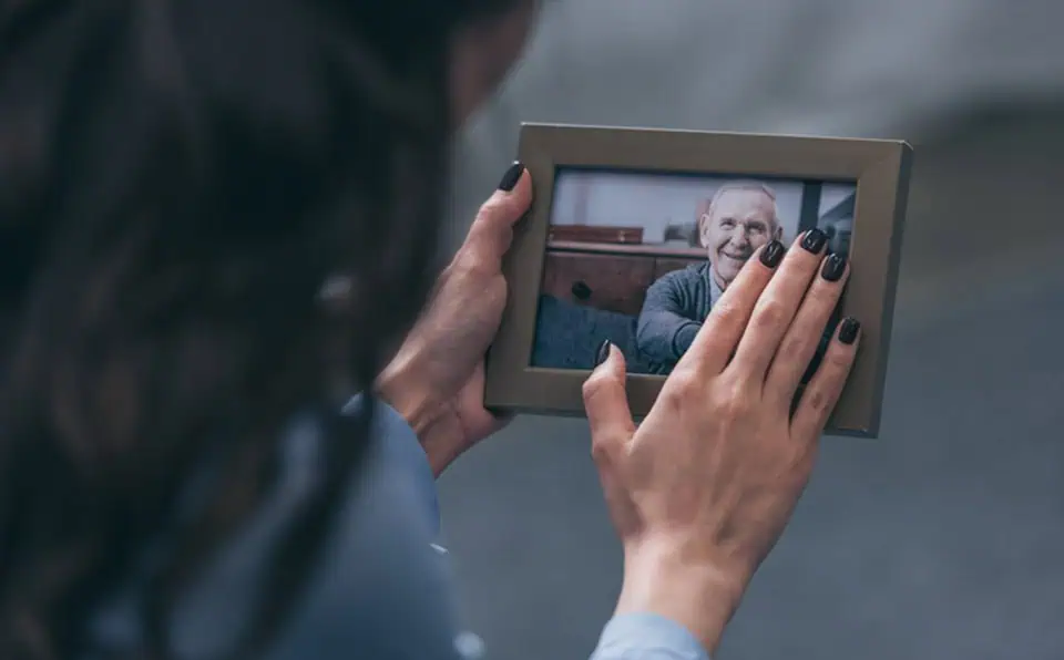 Person holding a framed photo of an elderly man with a warm smile.