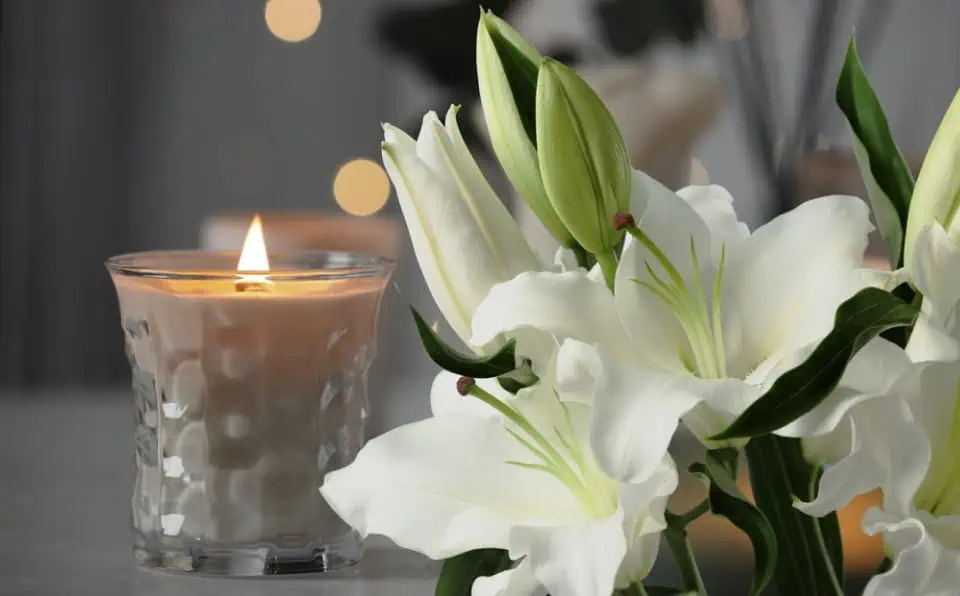 White lilies and a lit candle in a glass holder on a table.