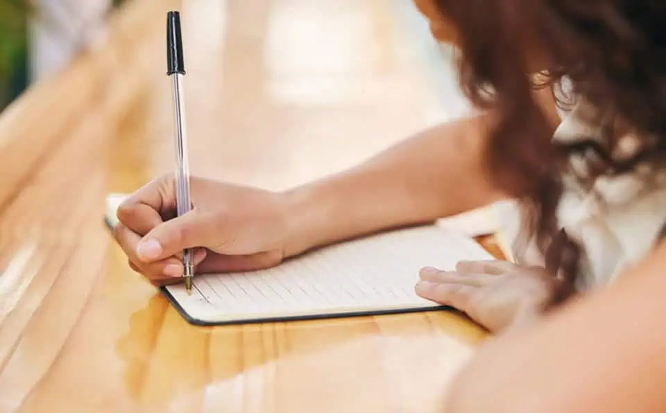 Person writing in a notebook at a wooden table.