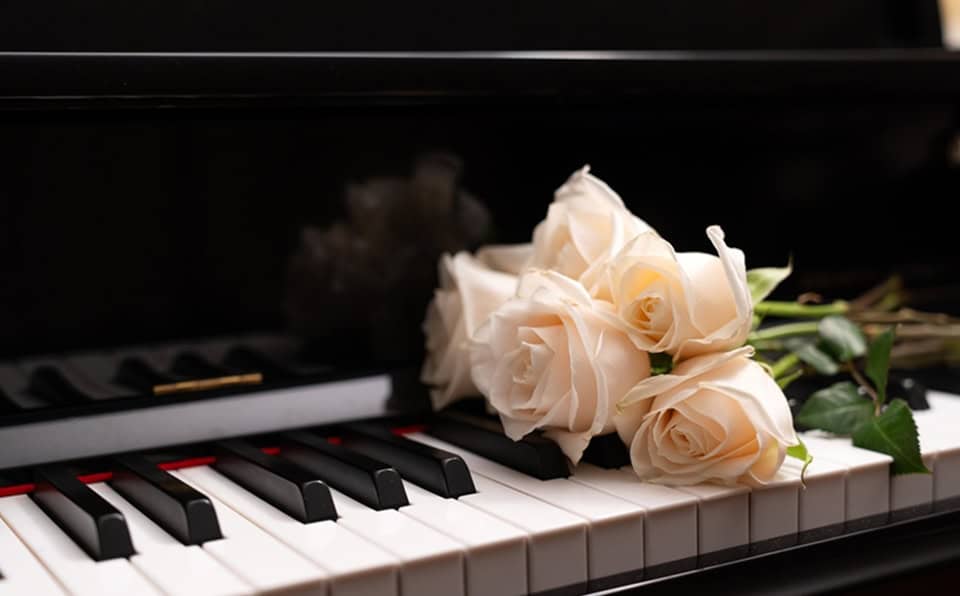 A grand piano with a bouquet of white roses resting on the keys.