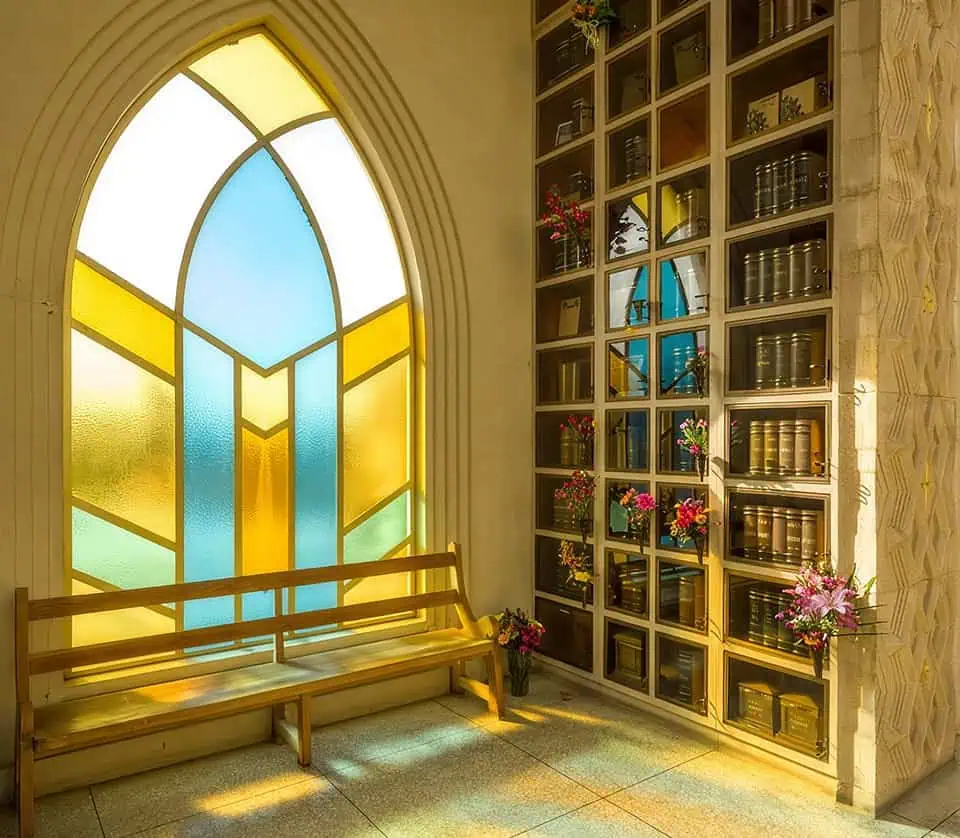 Colorful stained glass window beside a columbarium with flowers.