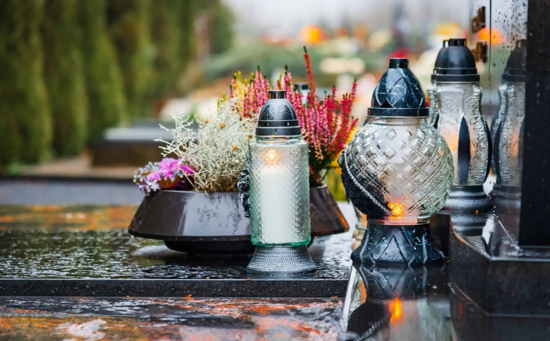 Memorial lanterns and flowers on a wet grave in a cemetery.