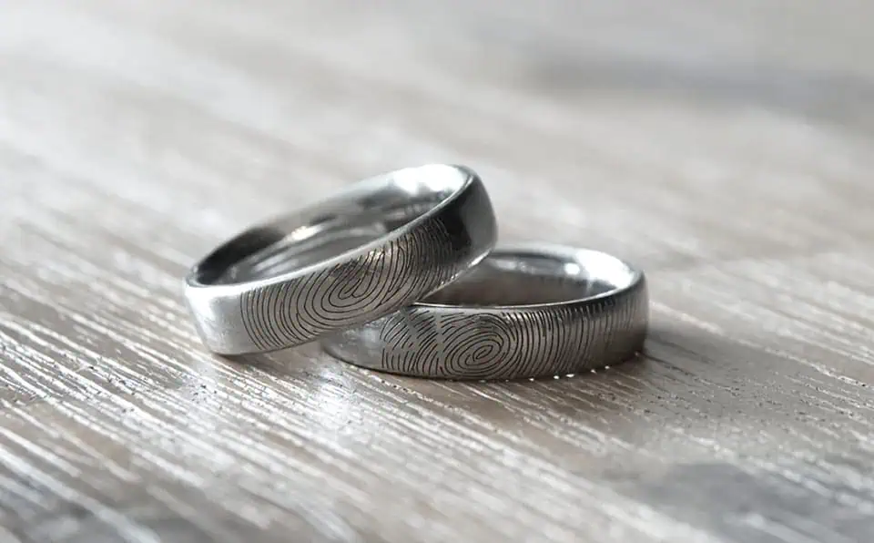 Two silver fingerprint jewelry rings on a wooden surface.