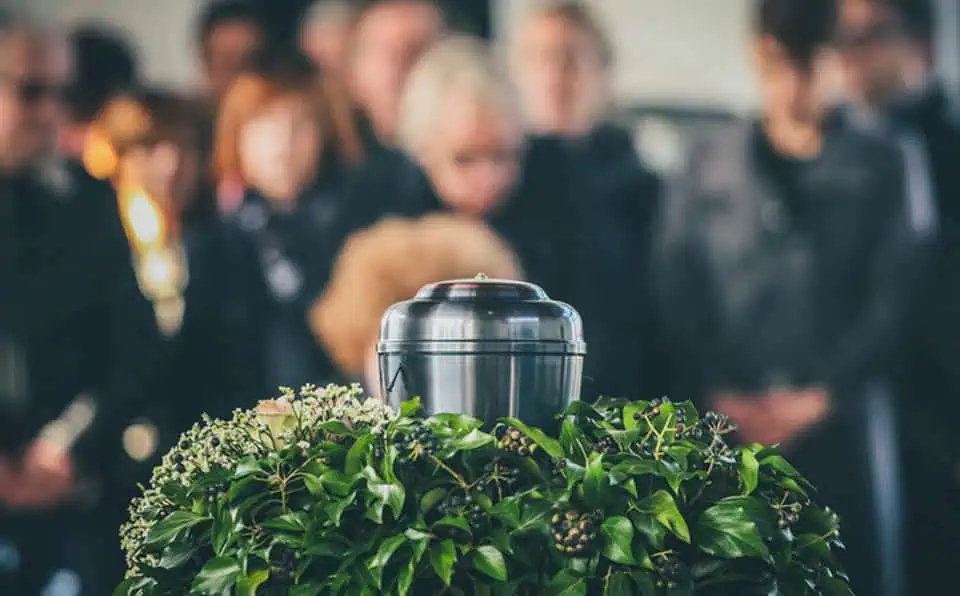 Cremation urn placed on a bed of green leaves and flowers at a memorial service.