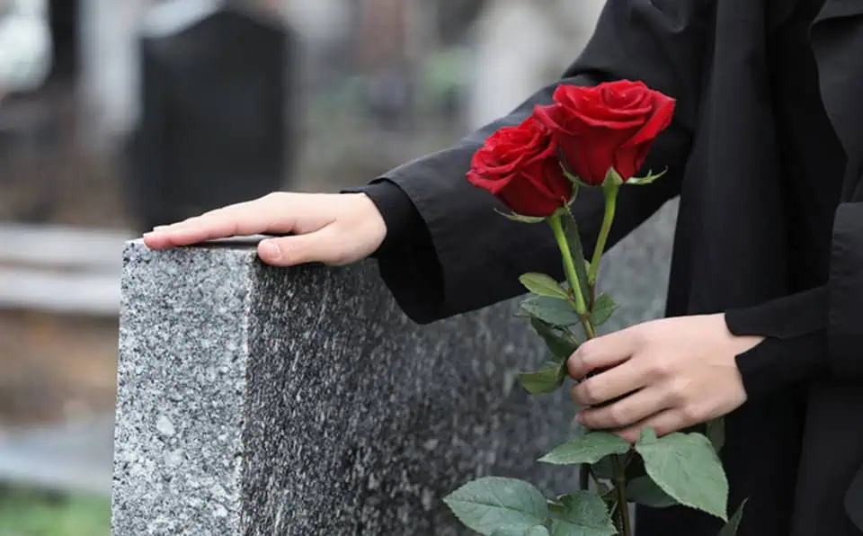 Person in black coat holding red roses at a cemetery.