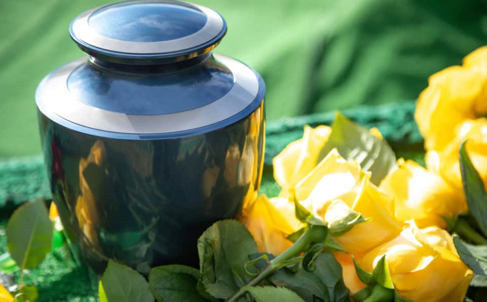 A polished black memorial urn surrounded by yellow roses on a green surface.