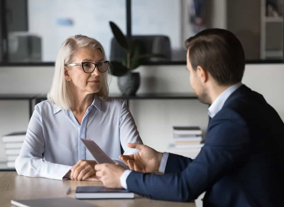 Older woman and young man discussing documents at a desk in an office.