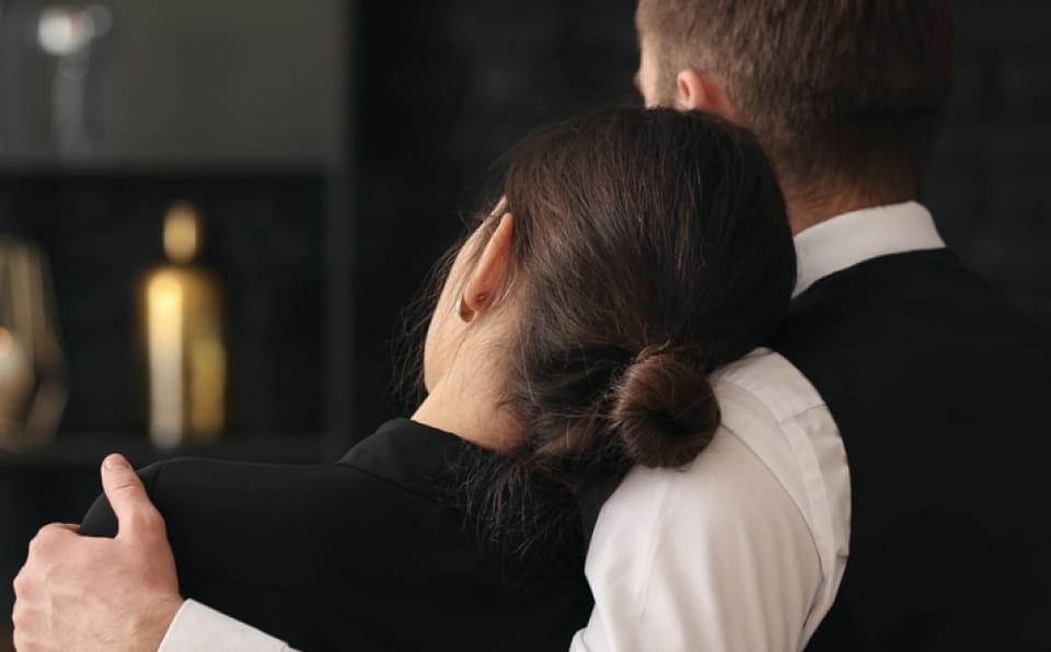 A woman and man share a comforting hug at a memorial service.