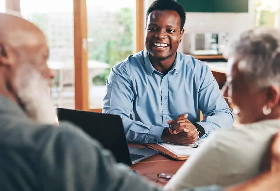 A young man discusses funeral arrangements with elderly clients in a bright room.