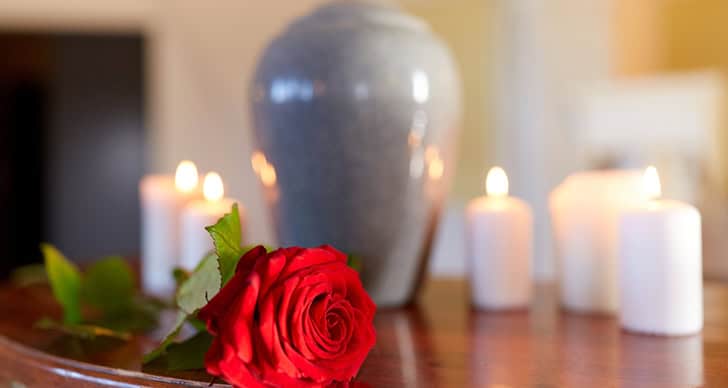A red rose and lit candles on a wooden surface with a vase in the background.