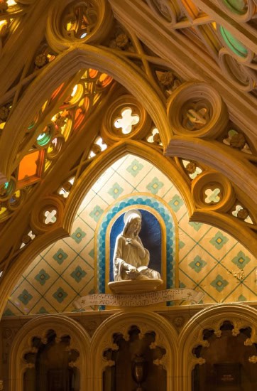 Colorful stained glass windows and a statue inside a chapel.