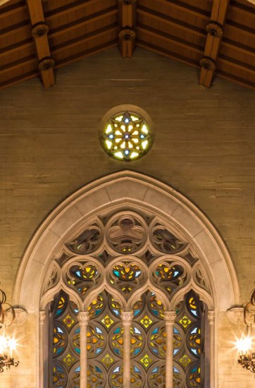 Interior of a chapel with stained glass window and wooden ceiling.