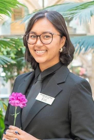 Smiling woman in professional attire holding a pink flower.