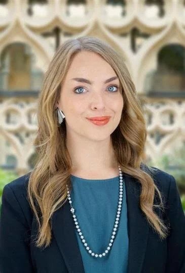 Portrait of a woman with long blonde hair and blue eyes, wearing a blue top and pearl necklace.