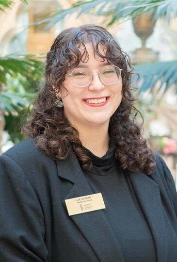 Smiling woman with glasses and curly hair in professional attire at memorial site.
