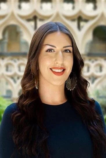 Portrait of a smiling woman with long dark hair and earrings at a chapel.