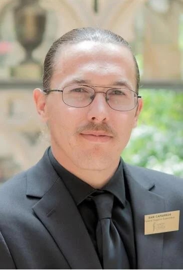Portrait of a funeral staff member wearing glasses and a suit with a name tag.