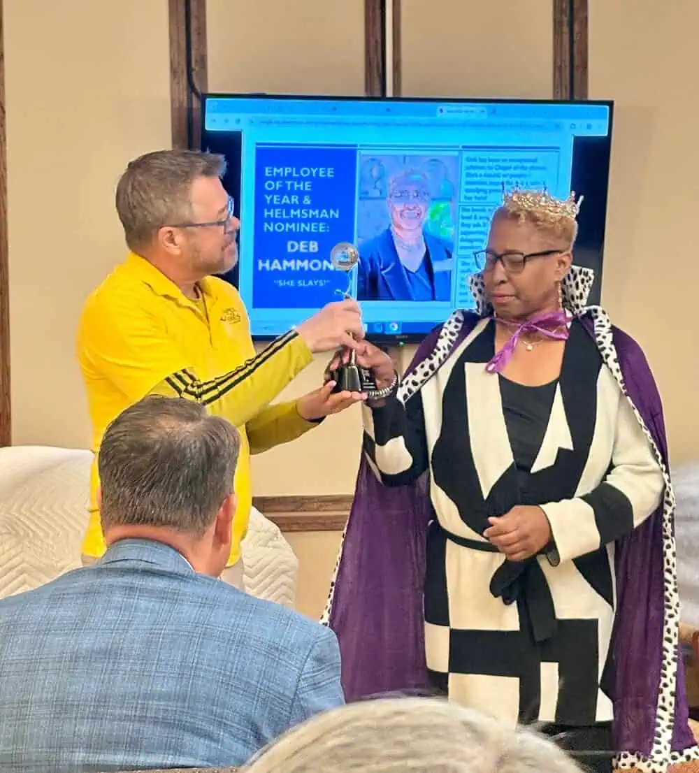 Man presenting award to woman at indoor event with screen in background.